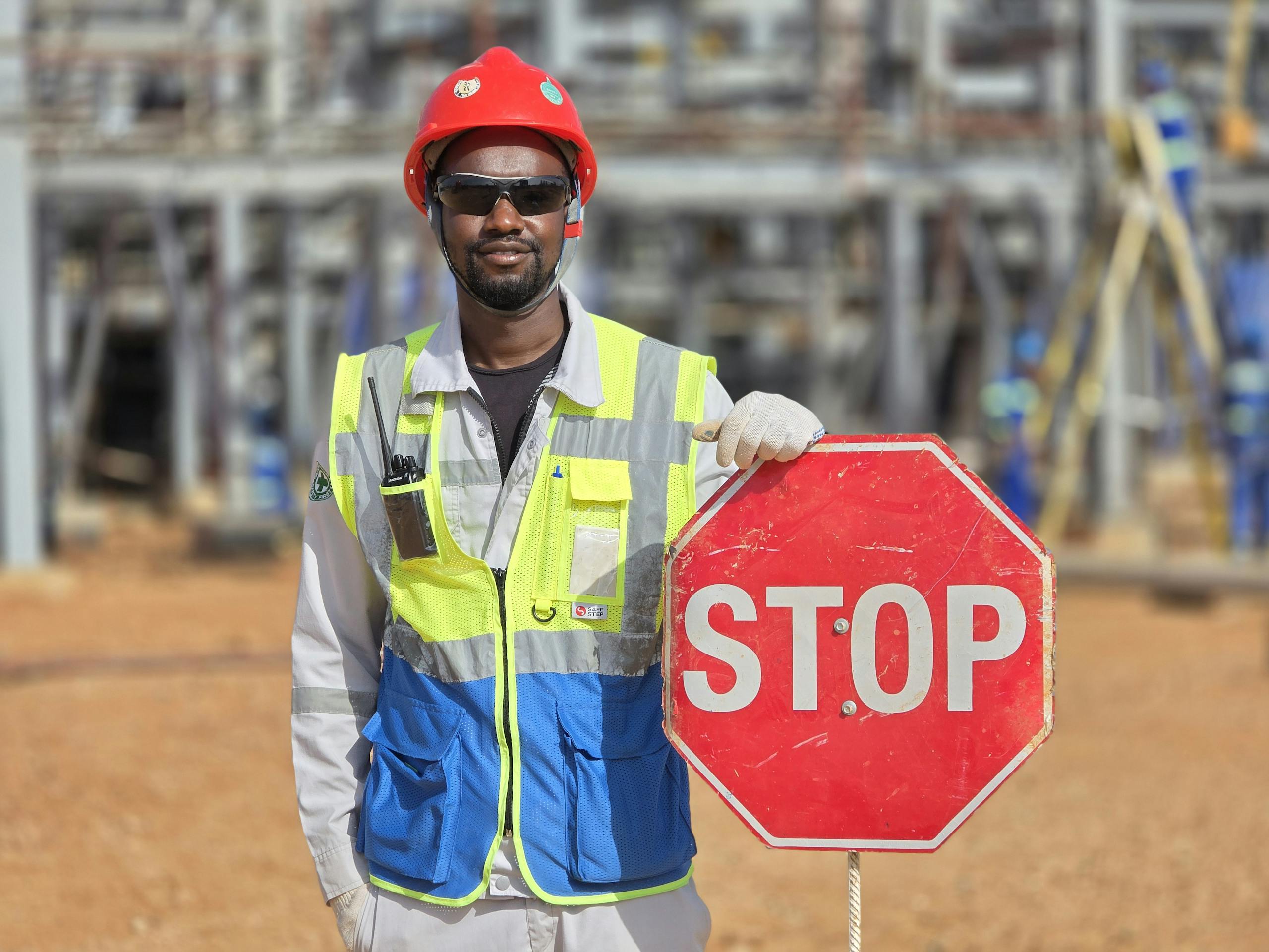 Construction worker in safety gear holding a stop sign at an outdoor construction site.